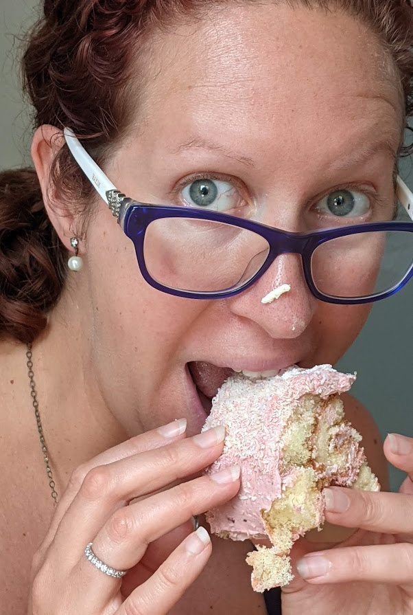 Woman eating pink frosted cake with her hands. Frosting smeared on her nose.