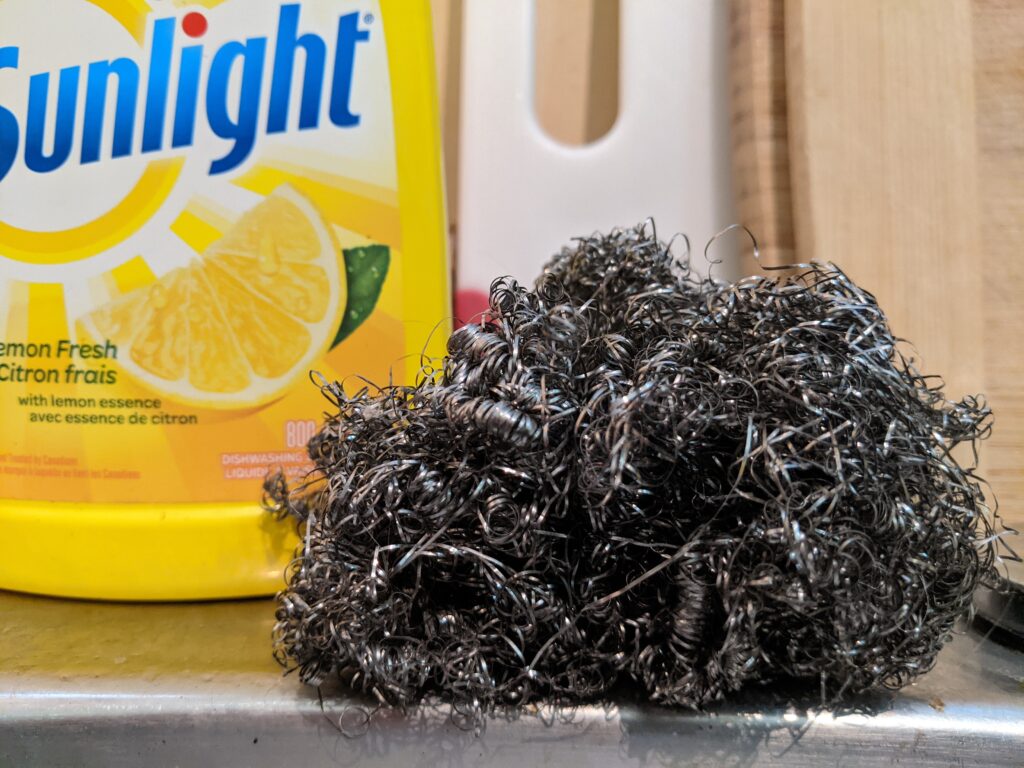 A curly and unruly steel wool next to dish soap