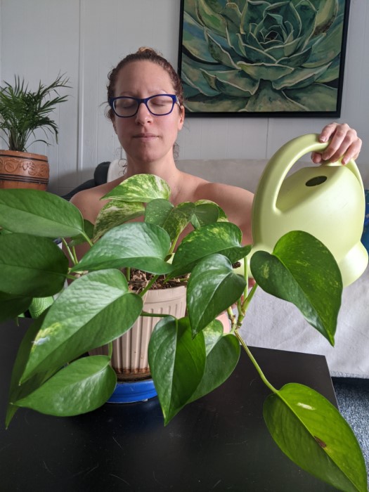 Nikki is watering a plant with a serene look on her face.