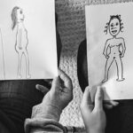 Women are holding exaggerated images they've drawn of themselves.