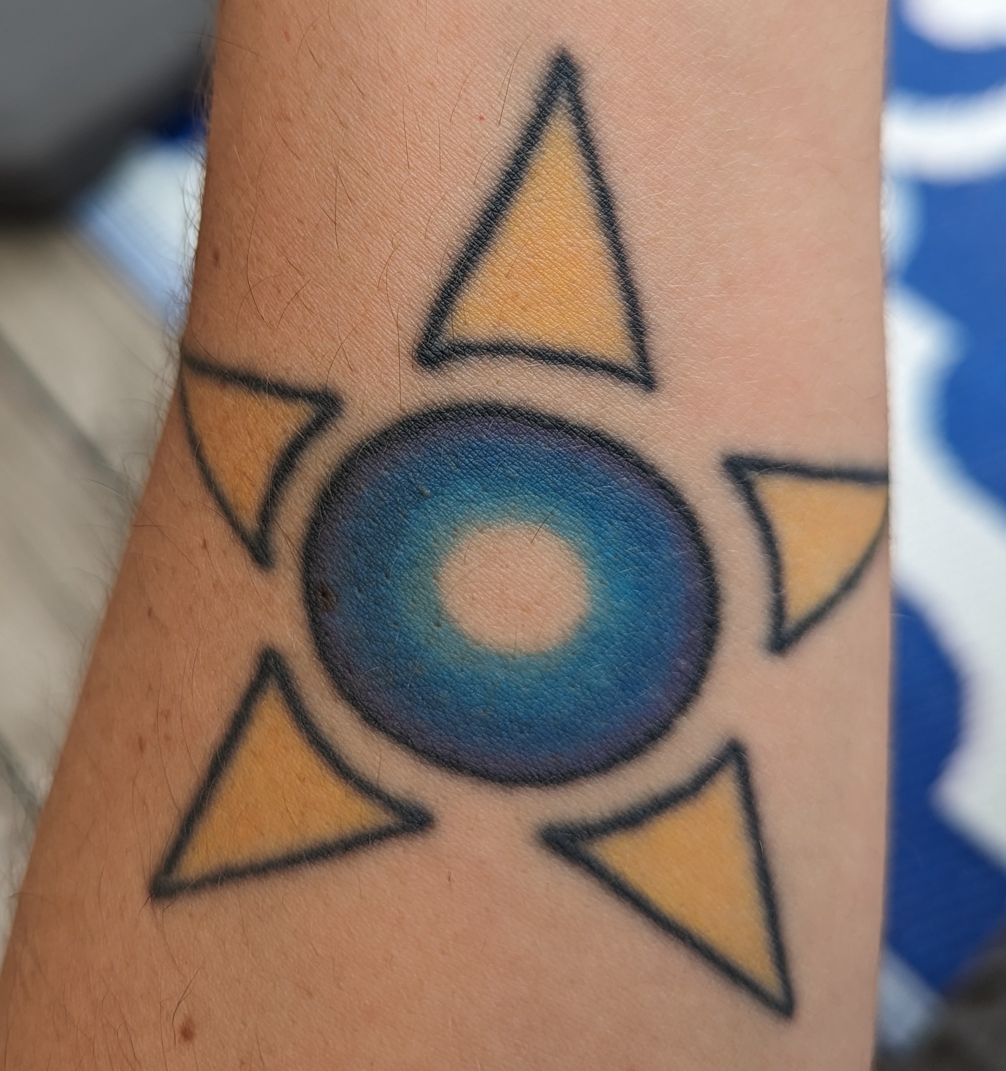 A tattoo of a thich colourful circle with beams of light coming from it making a star shape.