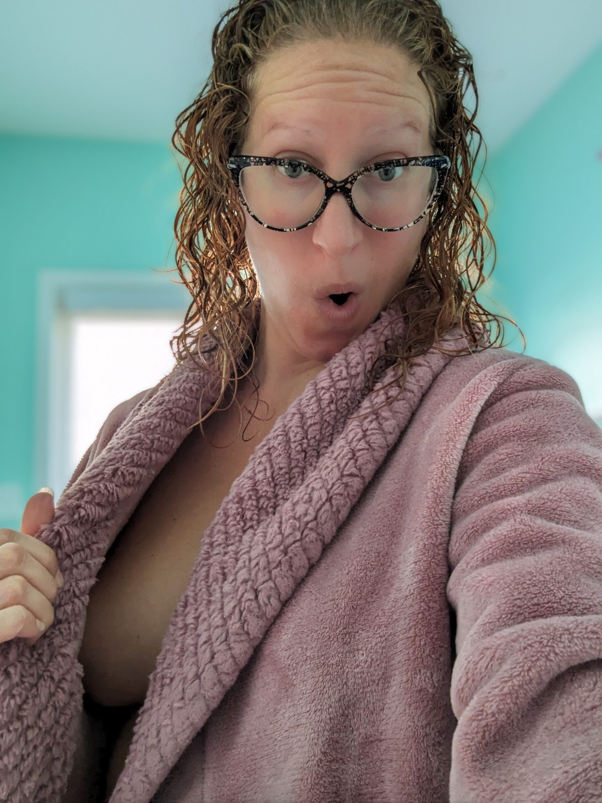 Nikki pulls her pink bathrobe aside to almost expose a breast. A cheeky expression on her face.